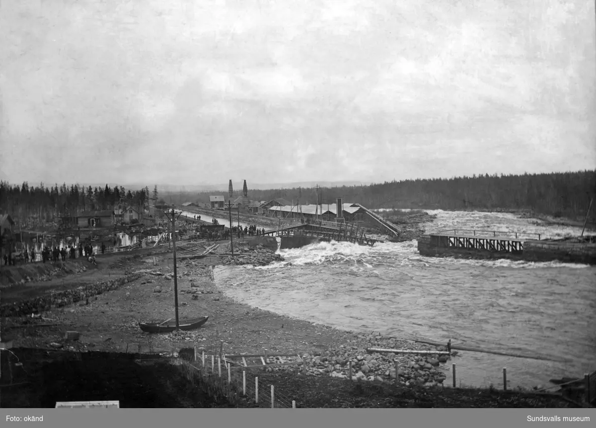 Alby kraftverksdamm våren 1906. En bristning i fördämningen har uppstått. I bakgrunden ses Alby karbidfabrik från 1901.
