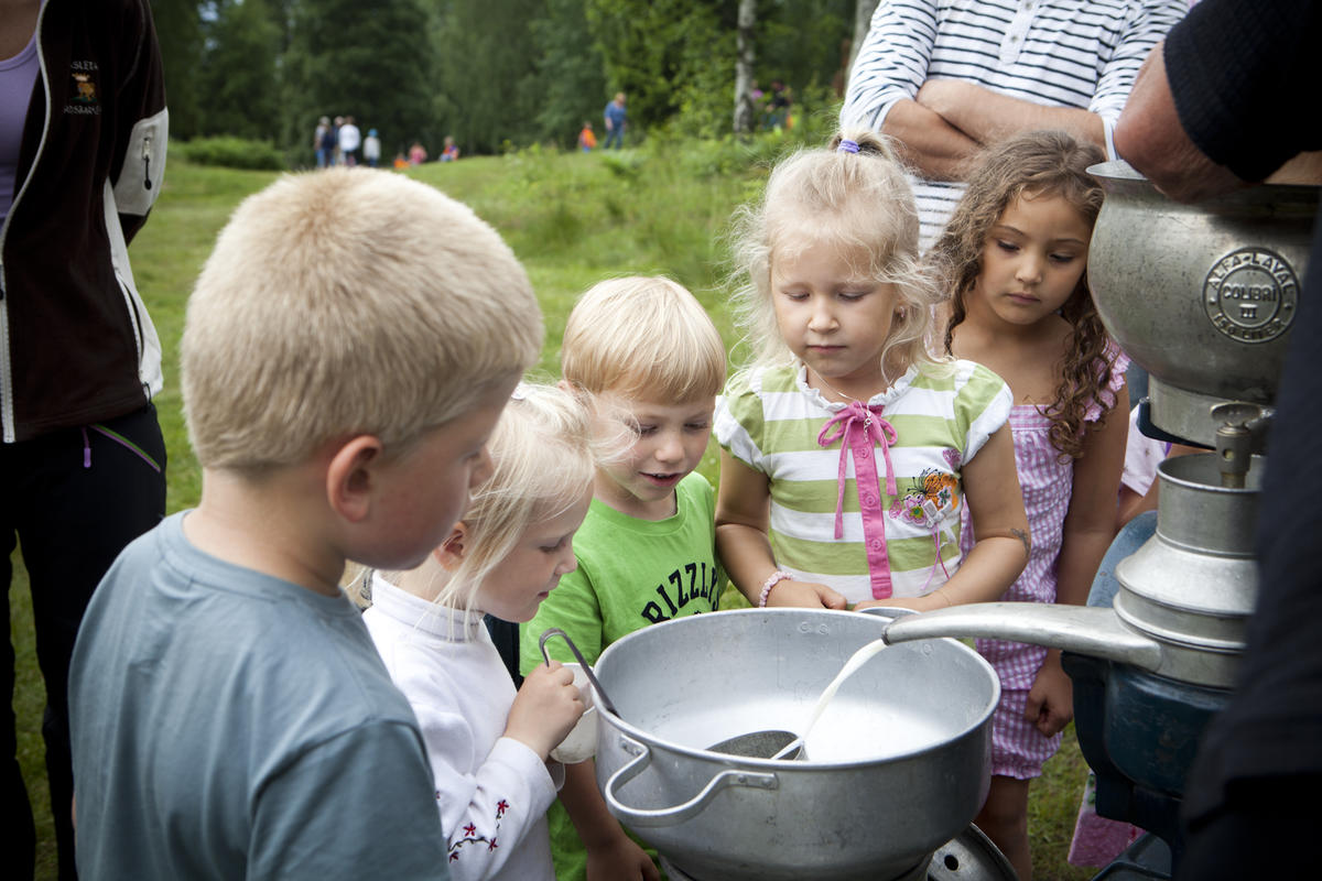 Flere barn som står rundt et melkeseparator og ser på hvordan melk separeres