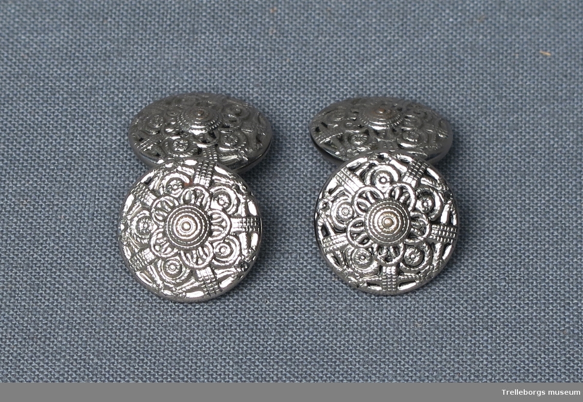Fyra stycken knappar av silvermetall, med tredimensionellt mönster i form av cirklar och streck, som bildar en blomma.
