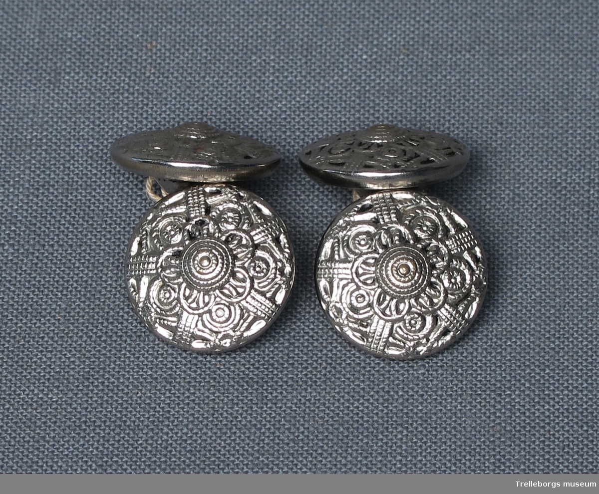 Fyra stycken knappar av silvermetall, med tredimensionellt mönster i form av cirklar och streck, som bildar en blomma.