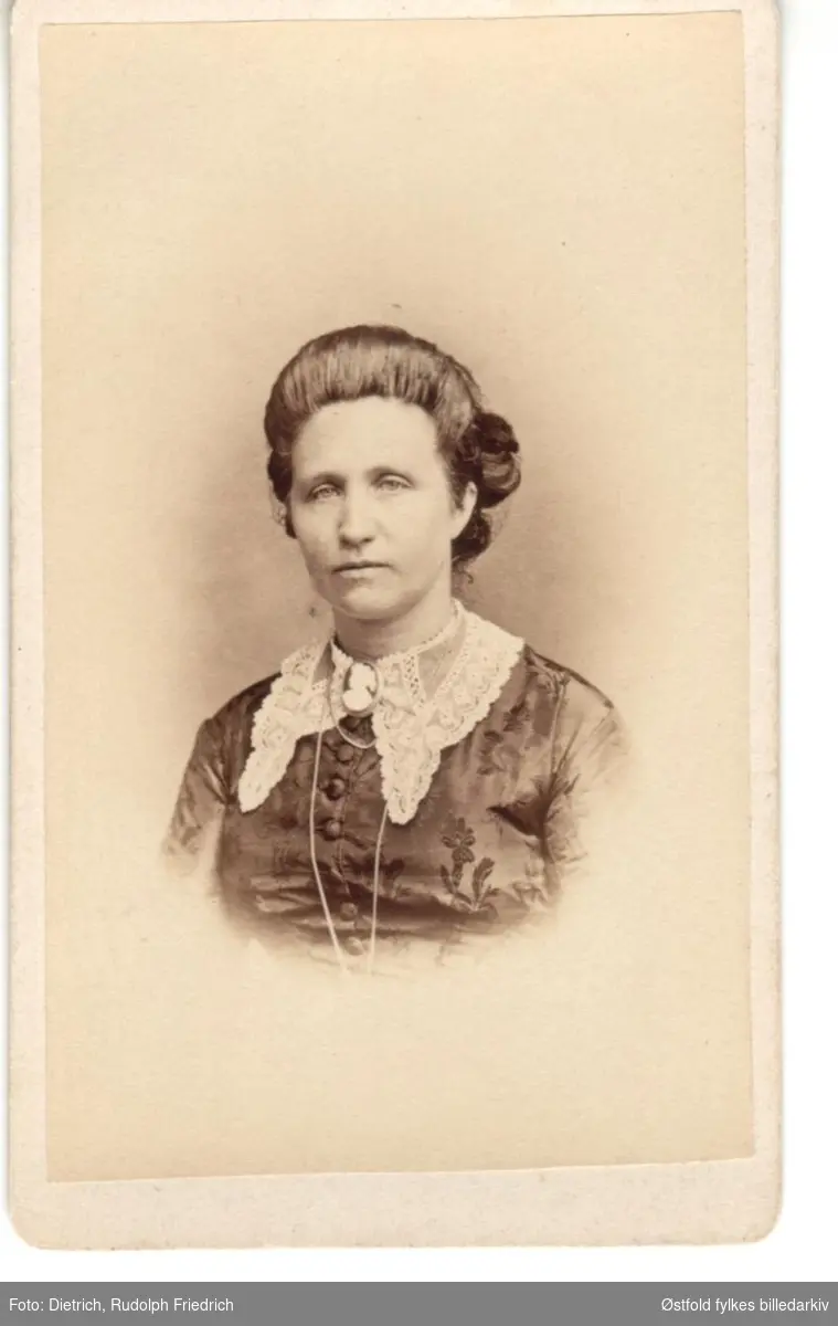 Portrett av ukjent kvinne, ca. 1865-1880. Vignettert. Antakelig fra Sarpsborgdistriktet. 
Visittkort med firmamerke.