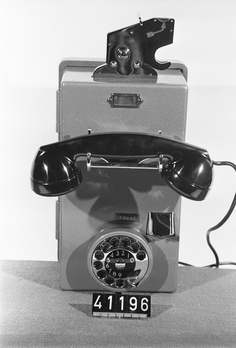 Telefonapparat CF 596, 10-öres myntapparat för AT-system. Väggmodell med grönlackerad plåtkåpa, mikrotelefon av bakelit modell m50 och fingerskiva av förnicklad mässing. Startavgiften är två 10-öringar, samtalet bryts efter en markering och vid obesvarat samtal återbetalas mynten. En ringklocka kan anslutas om apparaten ska användas för ankommande samtal.
