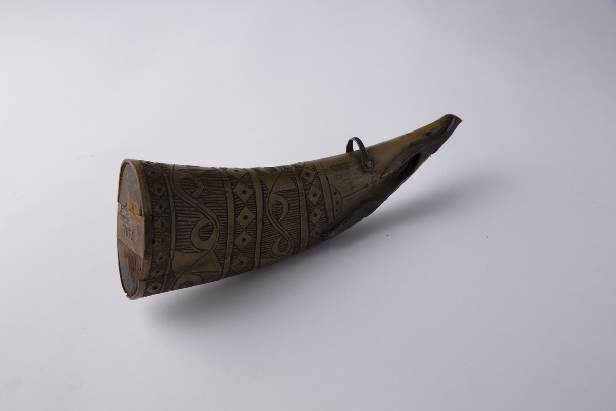 Krutthorn med bunnplate (med luke) i tre og lukkemekanisme og beslag i jern. Ornamentikk på horn i form av horisontale bårder.
