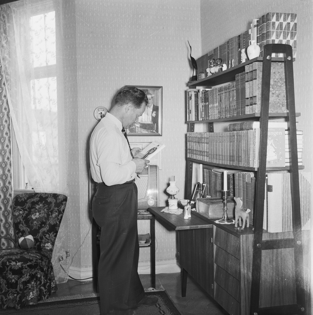 Interiör från fotograf Evert Anderssons hem på Odengatan 22 i Huskvarna. Evert står vid bokhyllan och har plockat fram en bok.