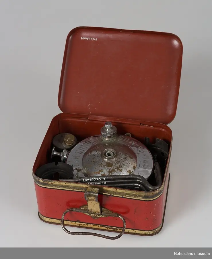 Primuskök med liten bränsledunk och nyckel och låda i metallplåt att förvara sakerna i. Lådan i röd färg och text "Primus" på locket.
