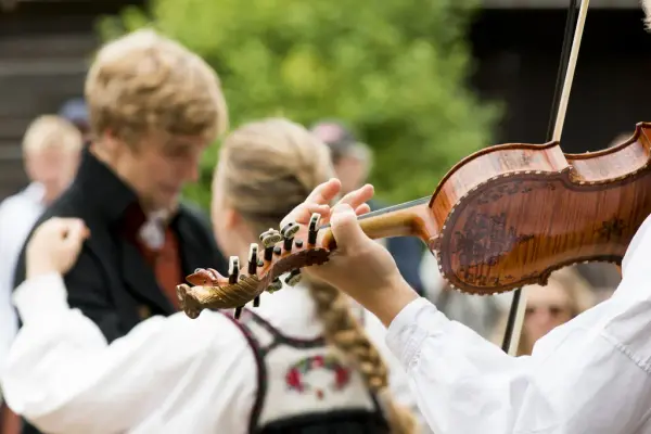 Nærbilde av par som danser folkedans og en som spiller hardingfele