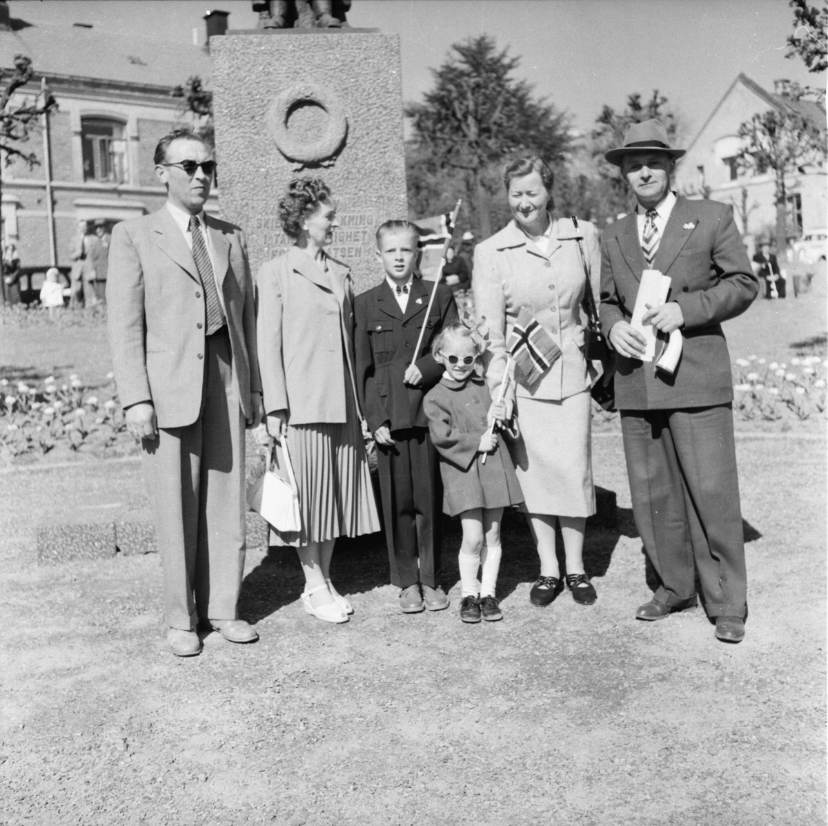 Vardens arkiv. "17 mai feiring. Seks mennesker fotografert foran minnesmerket for de falne i krigen 1940-1945 i Skien"  17.05.1954