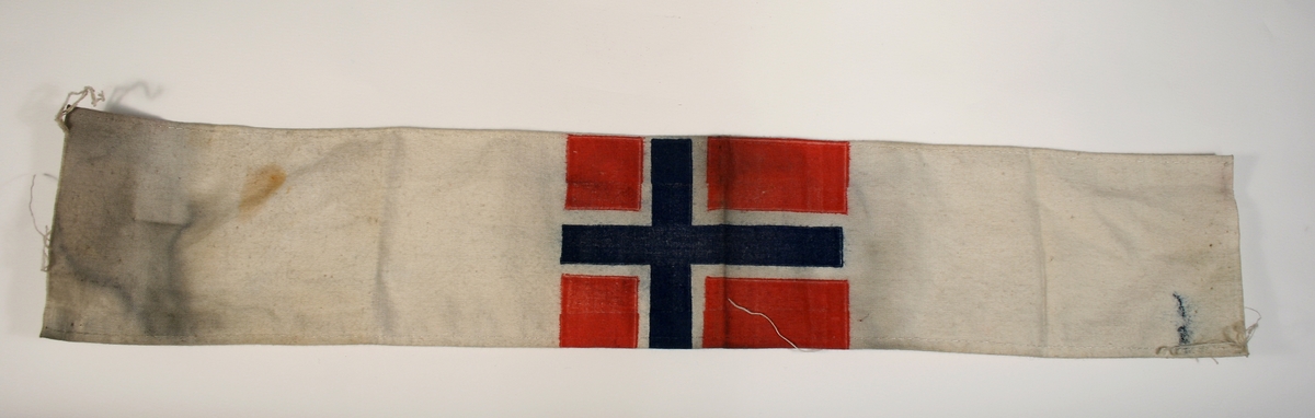Armbind i hvitt stoff med vit bunn med det norske flagget.