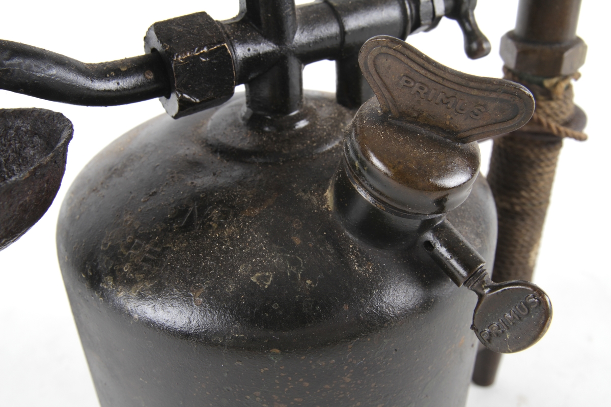 Blåselampe med tank med toppfylling, pumpe frittstående som handtak. Flammedelen er montert på toppen av tanken. Tvinnet tau rundt pumpe/handtak.