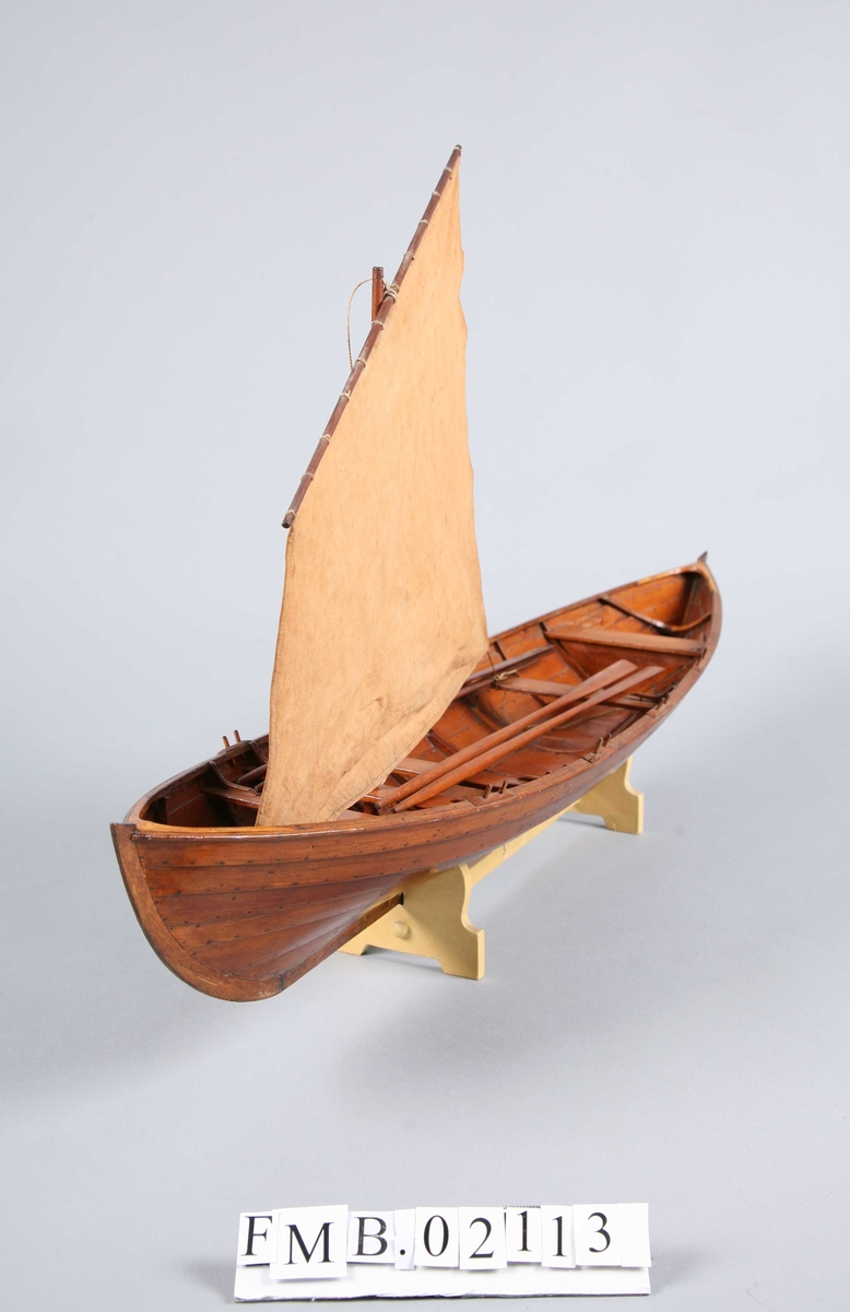 Sjekte med mast, seil og 4 årer. Den har 6 par tollepinner. Båtmodellen står på en støtte (krybbe).