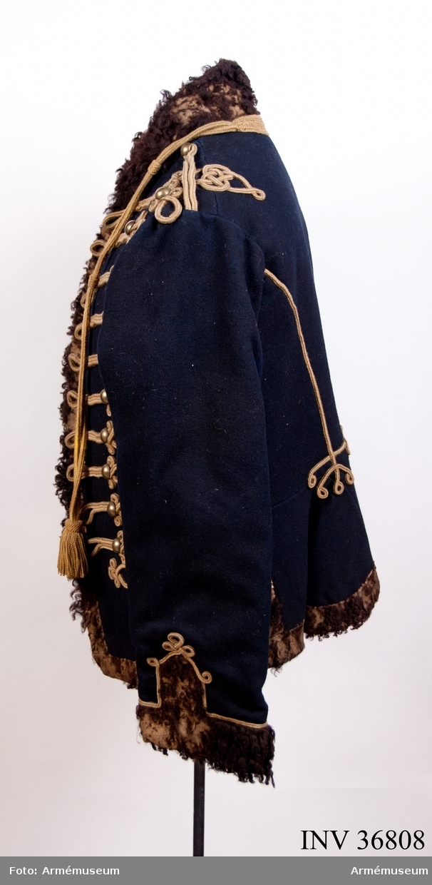 Grupp C I.
Dolma av mörkblått kläde med krage och ärmuppslag av svart fårskinn samt snören av gult ullgarn.