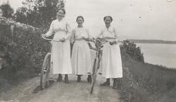 Tre kvinner med sykler, fotografert på en vei.