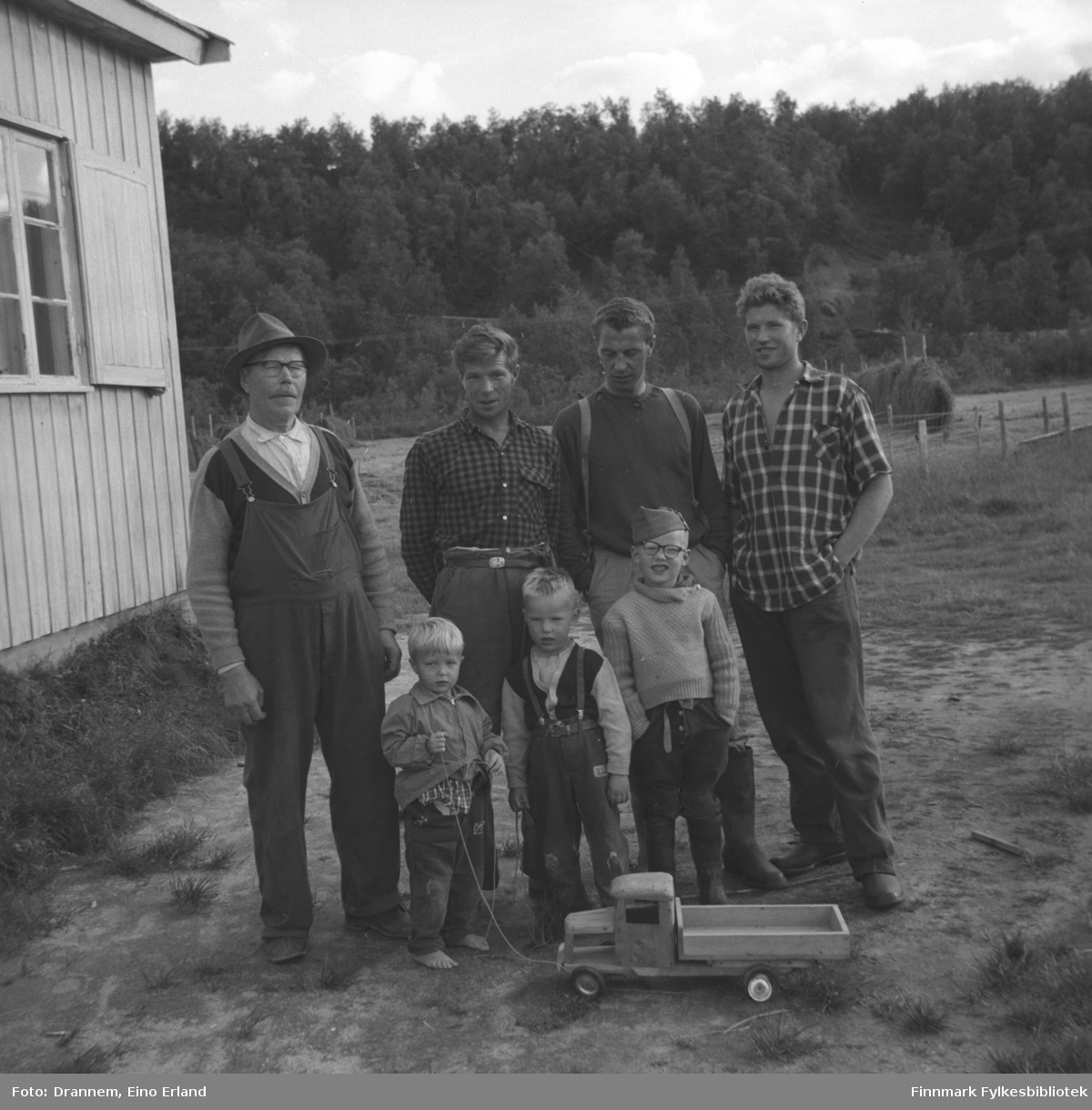 Fire menn og tre gutter fotografert på gårdsplassen ved langveggen til et hus. De er fra venstre, Alfred Karikoski, Aage Karikoski, Jacob Karikoski, og Oskar Karikoski. Navnet på guttene foran er ukjent.