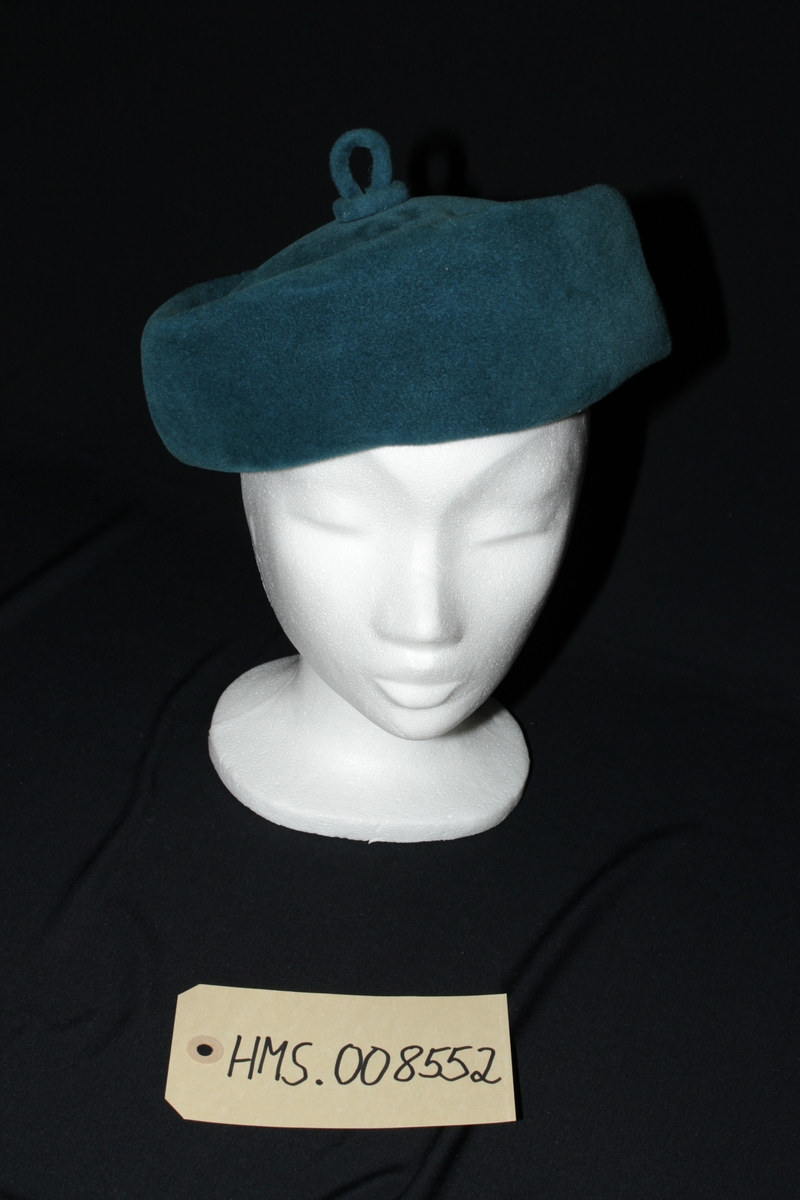 Mørk turkis damehatt med en hempe i samme stoff og farve på toppen av hatten