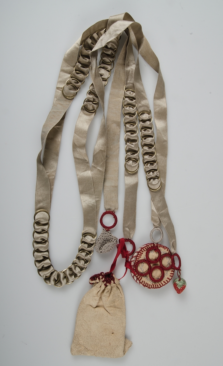Beigefärgat silkeband, dubbelt, med sämskskinnspung, nålbok, smultron och liten virkad pung fäst i olika ändar.

