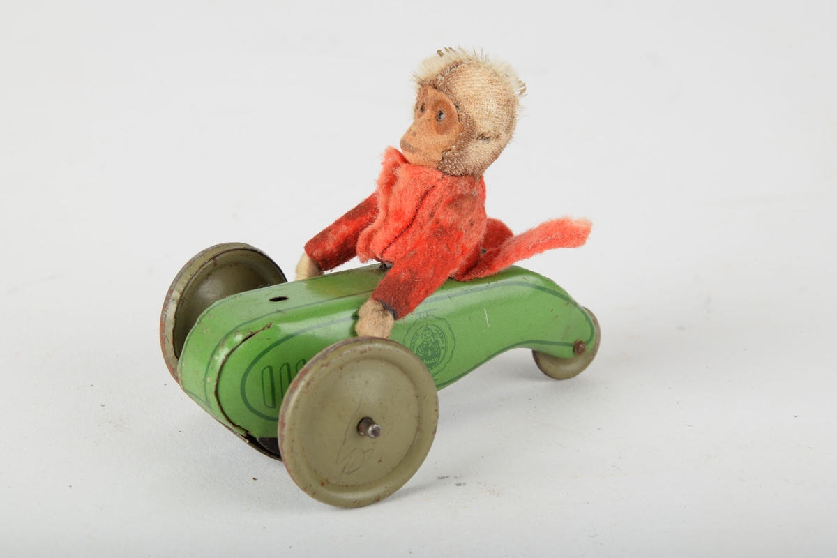 Mekanisk leketøy av en lekebil med apekatt i tøy som sjåfør. Mekanikken har trolig drevet hjulakslene rundt.