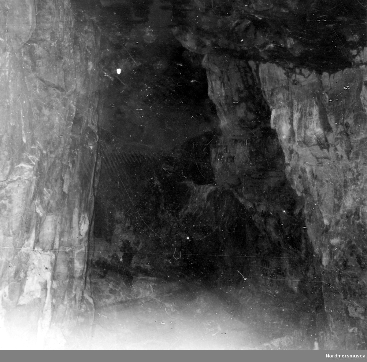 Foto, tatt med blitzlampe inn i Bremsneshula.  Som en ser ble ikke fotoet klart selv med blitzen.  Jeg sto ved indre steinvoll.  En ser tydelig bergveggene til høyre og til venstre.  En ser også indre hula som et mørkt parti øverst til høyre.  Stigen opp til denne er skjult av bergveggen foran.  
Så ser vi det store mørke parti i midten:  Innover til indre hula i nordøst der
"sau-beinet ?" ble oppgravd, og en skimter   bergforøhyningen foran innerste hulerom nederst.  (Se Yderstads notater i bind 10 side 203 ff).
Fra Nordmøre Museums fotosamling.