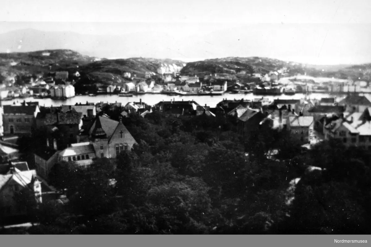 Utsikt fra Kirkelandet Kirke og Kirketårnet som stod på Lyshaugen, på Kirkelandet i det gamle Kristiansund. Her ser vi mot havnen og Torvet. I bakgrunnen ser vi Nordlandet. Fra Kristiansunds fotosamlinger.
