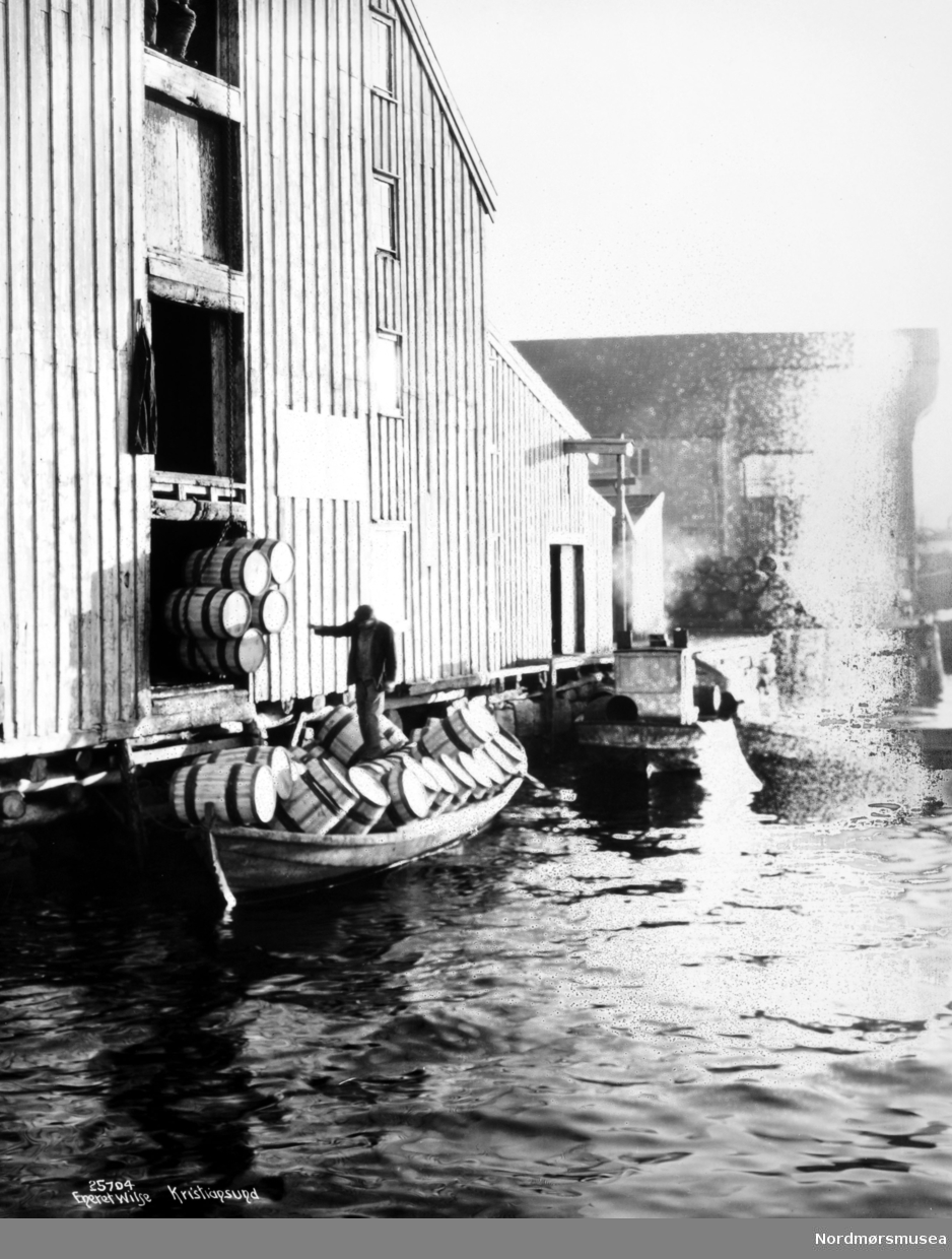 Her laster man tønner med saltet sild ombord i en ventende båt ved brygga, for frakt. Bildet er trolig fra perioden 1910-1930, trolig fra Werringbrygga på Kirkelandet i Kristiansund. Fra Nordmøre Museums fotosamlinger.

Her laster man ikke tønner med sild om bord i en båt. Man enten losser tomtønner fra en færing, eller laster om bord tomtønner. Hadde tønnene vært fylt med sild, ville båten sunket. Nå flyter den lett på vannet med mange tønner om bord. (Tilleggsinformasjon fra Aslak Kristiansen.)



