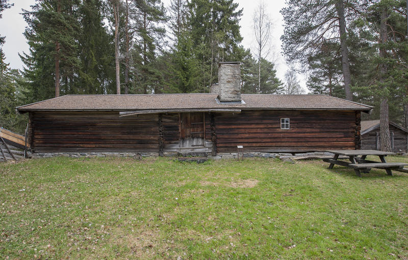 Langt størhus i brunlig tømmer, med stor plen og et parkbord utenfor. (Foto/Photo)