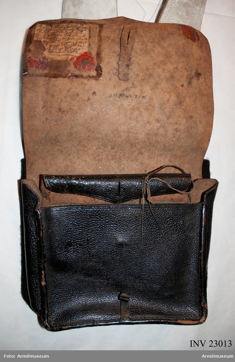 Patronväska av svart läder, med inredning av bleckplåt. Samhörande bandolärrem (modellpersedlar).
Bleckplåtsinredningen har plats för 6 stycken patroner, ett smörjehorn, fängnålsknippet och ett kruthorn.