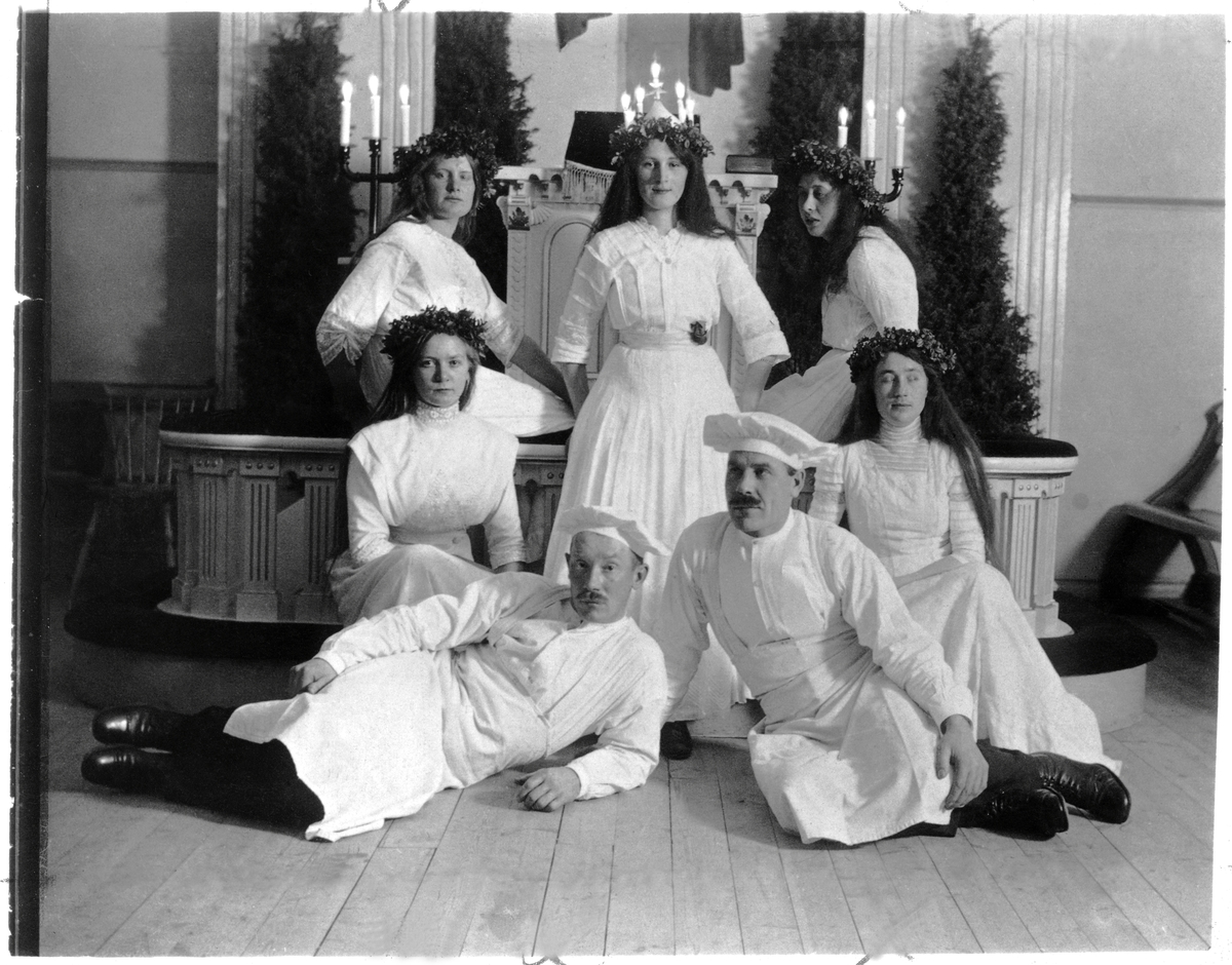 Västerås första Lucia, Anna Palm, från 1914, omgiven av tärnor och bagare. Festen hölls i stadens metodistförsamlings kyrksal. Bagaren till vänster är en av männen, fd Göteborgare, som planerade festen.