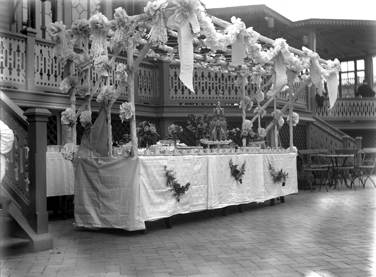 Foto av ett uppdukat och garnerat buffébord med kaffekoppar i mängder, blomvaser och en stor krokan, utanför Societetshuset.