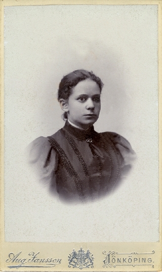 Porträtt (bröstbild, halvprofil) av en ung kvinna i mörk klänning med hög sammets(?)-krage och snörmakerier på livet.