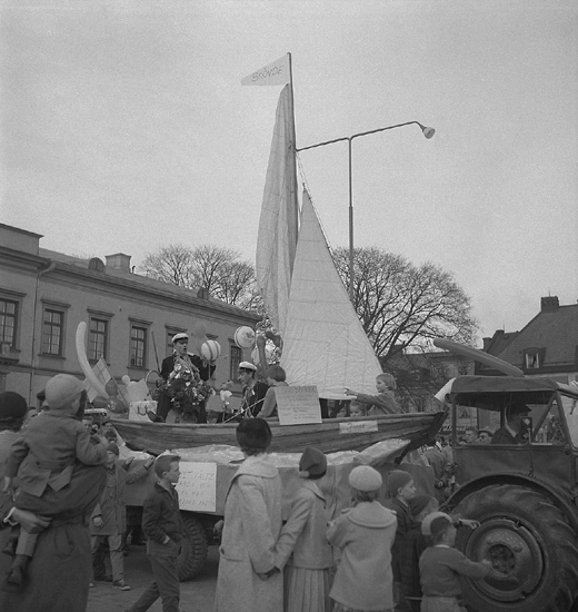 Studenterna sista dagen, 14/5 1958. 
Några studenter i en segeleka på Stortorget. I toppen på masten syns en vimpel med texten: "Skövde". 
I bakgrunden skymtar Residenset.