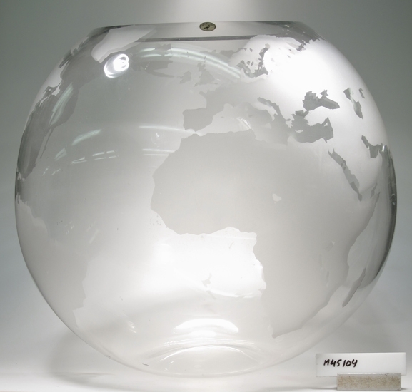 Glasskulptur.
Jordglob av ofärgat glas, med mattblästrade kontinenter.
Klotformad med öppen mynning.

Klarglas.

Rund etikett med en trana på och ordet " Transjö".
Funktion: Prydnadsföremål/ (vas ?)