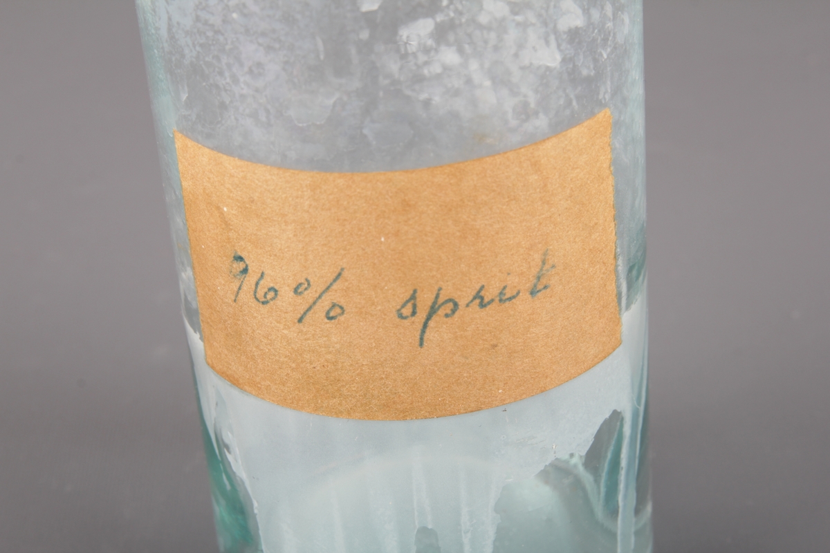Sylindrisk glassflaske med etikett og kork. Brukt til oppbevaring av 96% sprit.