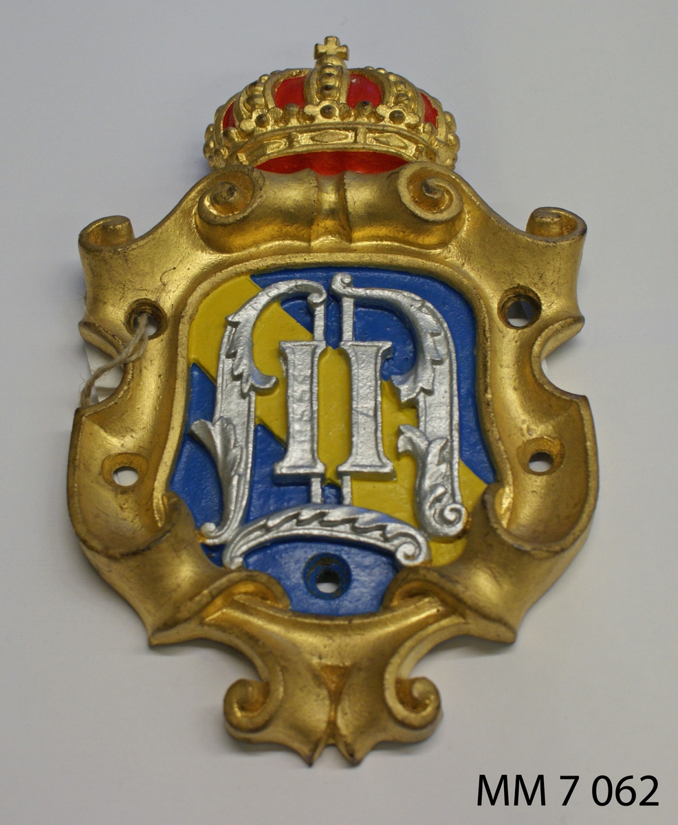 Utgöres av sköld med kungl. krona. Inom skölden på en blå botten finns ett band i gult med kung Oscar II:s bronserade namnchiffer. Kanterna på skölden är förgyllda. Kronan är förgylld och målad i rött.