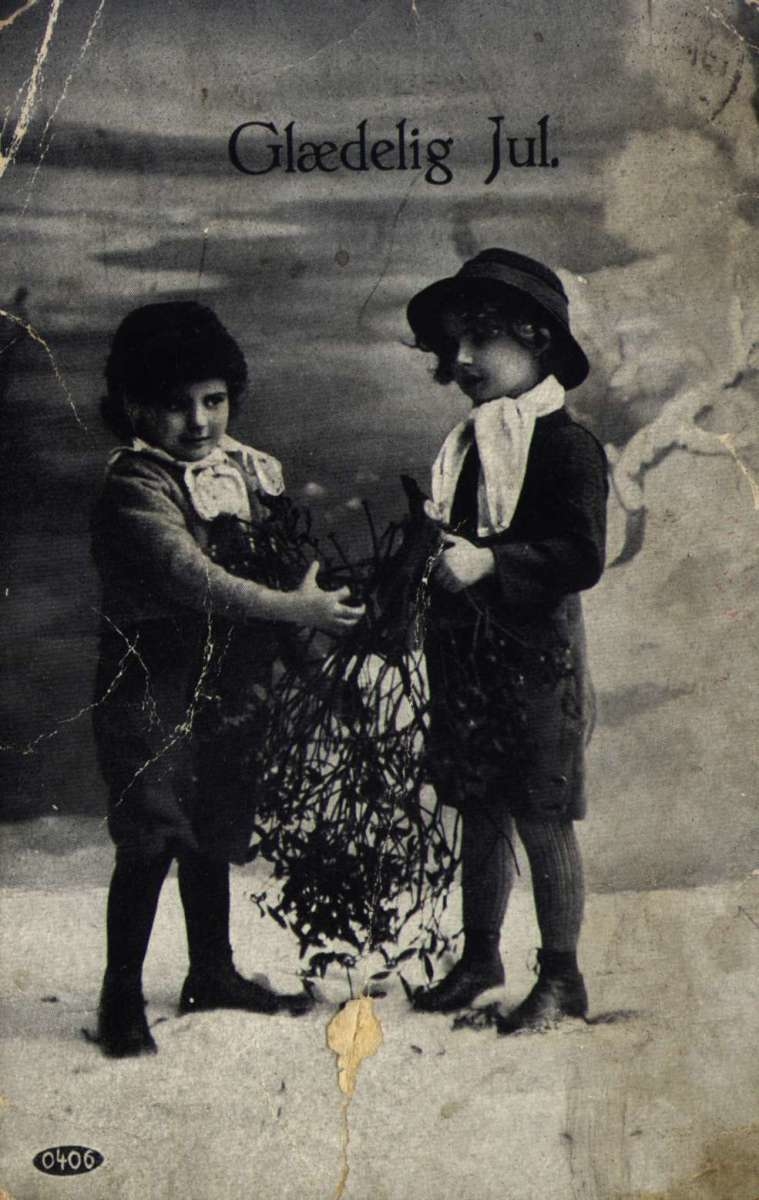 Julekort.  Fotografisk motiv. Svart/hvitt. To barn står og holder på noen greiner. Landskap med vann i bakgrunnen. Påskrift 22.12.1916.