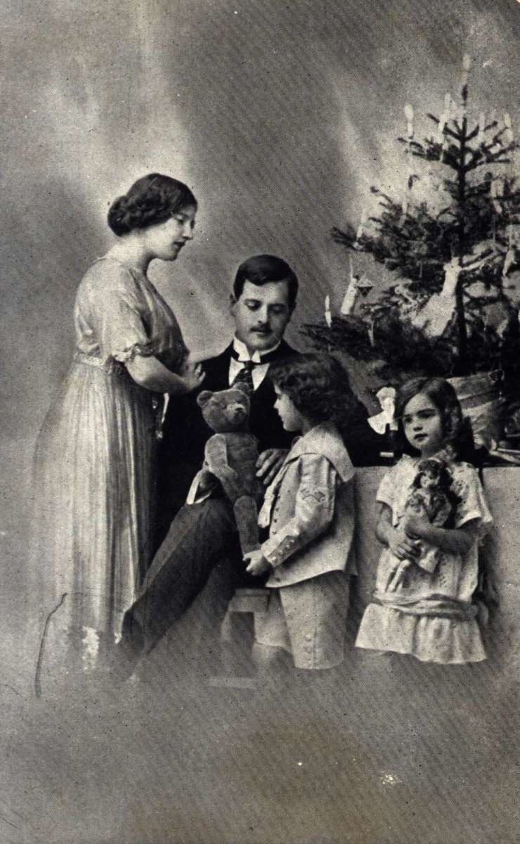 Julekort. Jule- og nyttårshilsen. Svart/hvitt fotografi. Far, mor og to barn foran juletreet.