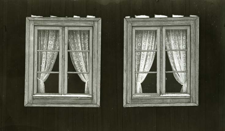 Två fönster med gardiner invändigt och foder utvändningt.