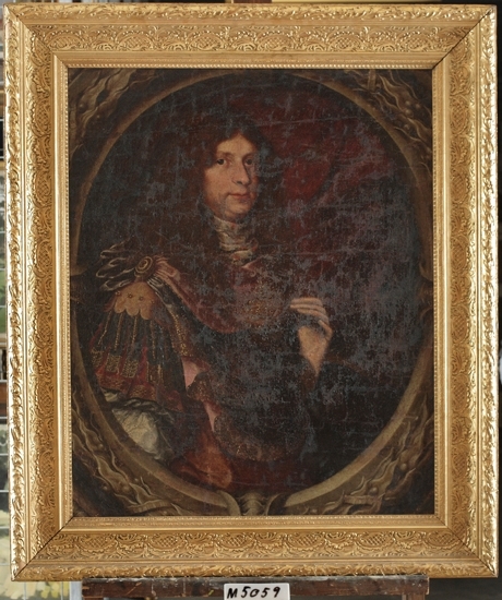 Oljemålning på duk.
Porträtt föreställande manlig ståndsperson med mörk peruk och romersk uniform.
Mörkbrun bakgrund inom delvis synlig oval av lager.
Skall enligt uppgift föreställa kung Fredrik I (?) (1676-1751) .