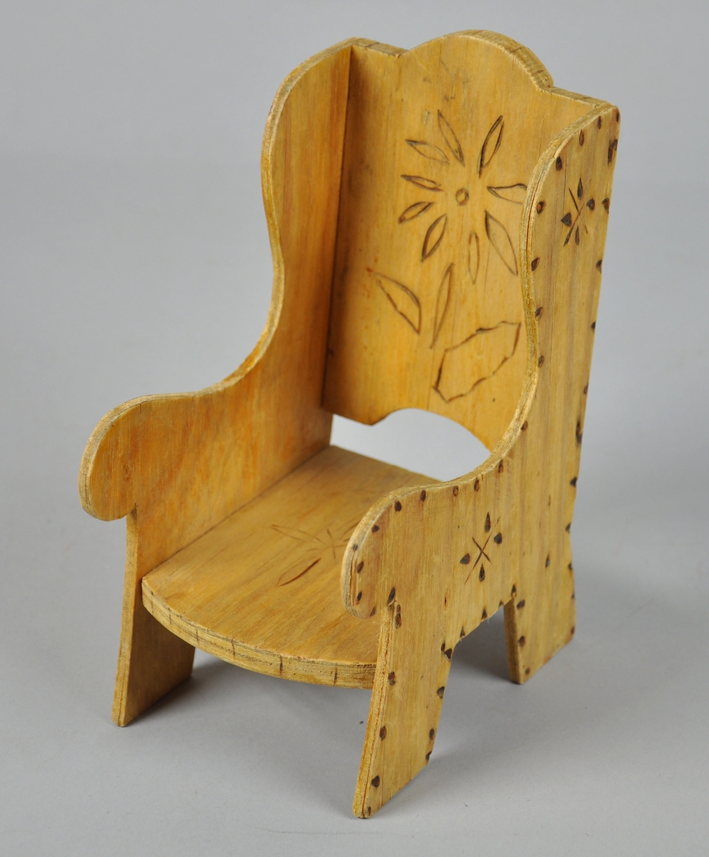 Dukkestol laget av finér. Stolen har svidekor i rygg, sete og sidestykkene.
