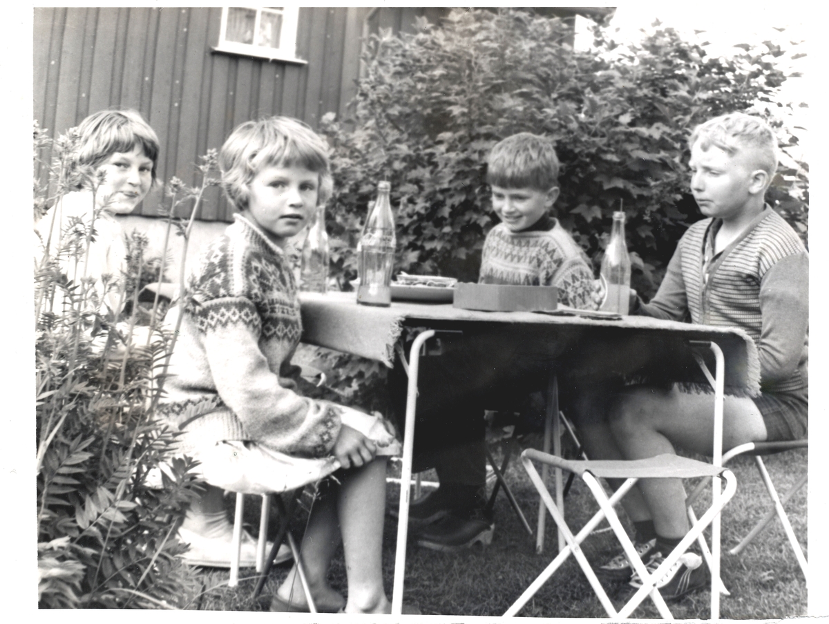 4 barn koser seg i hagen med brus. Sommer