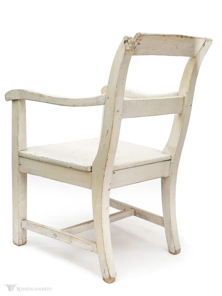 Hvitmalt barnestol i tre med rett fasong.  Stolen har 2 armlener og 1 tverrsprosse i ryggen.