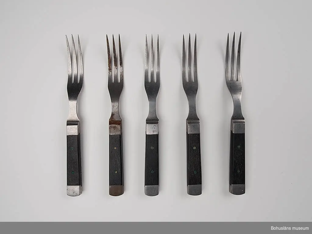 Trekloig gaffel med svart träskaft. I skaftets båda ändar metallskoning, 5 st.
Snarlik UM017095 och UM017096. Snarlik kniv UM017098:1-4.