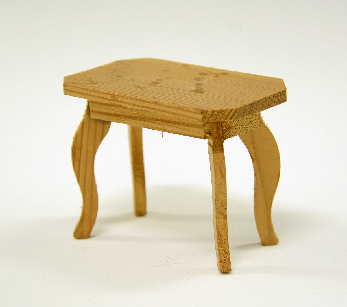 Miniatyrbord rektangelform, men hjørnene på bordplata er saga av, så bordplata har åtte kanter. Bordet har svungne ben.
