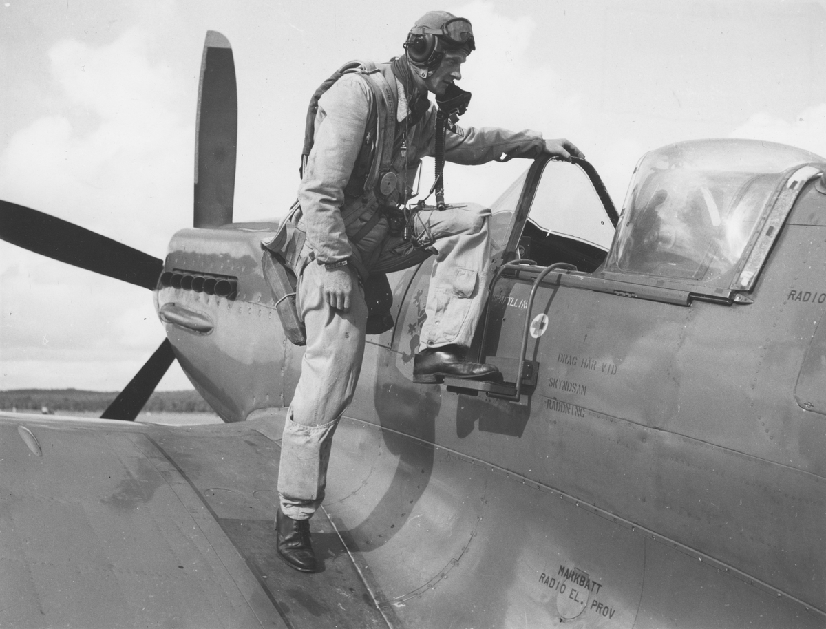En man klädd i flygardräkt kliver in i flygplan S 31 Spitfire.