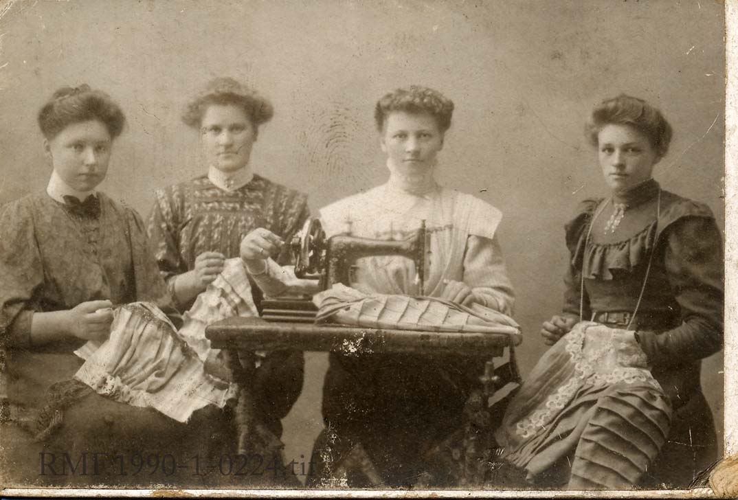 Fire unge kvinner som poserer med symaskin og sømarbeid, drakt. Syersker.