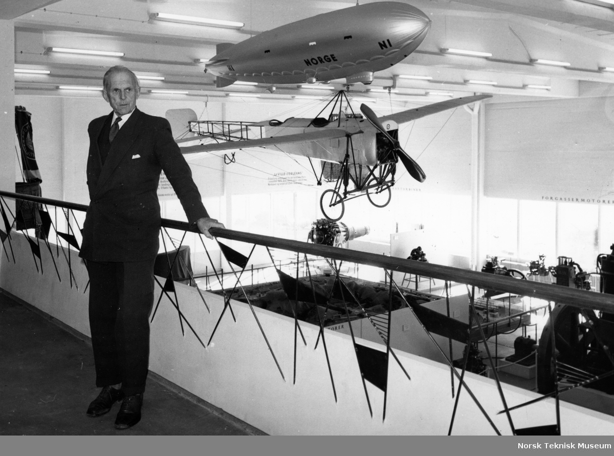 Tryggve Gran besøker flyutstillingen på Norsk Teknisk Museum på Helsfyr. Han står på galleriet, i bakgrunnen hans eget fly "Nordsjøen" og en modell av Roald Amundsens luftskip "Norge". 20.4.1961.