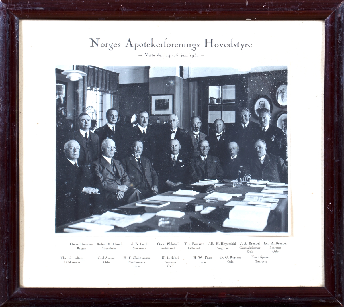 Gruppefoto av 15 voksne menn i dress sittende rundt et møtebord.