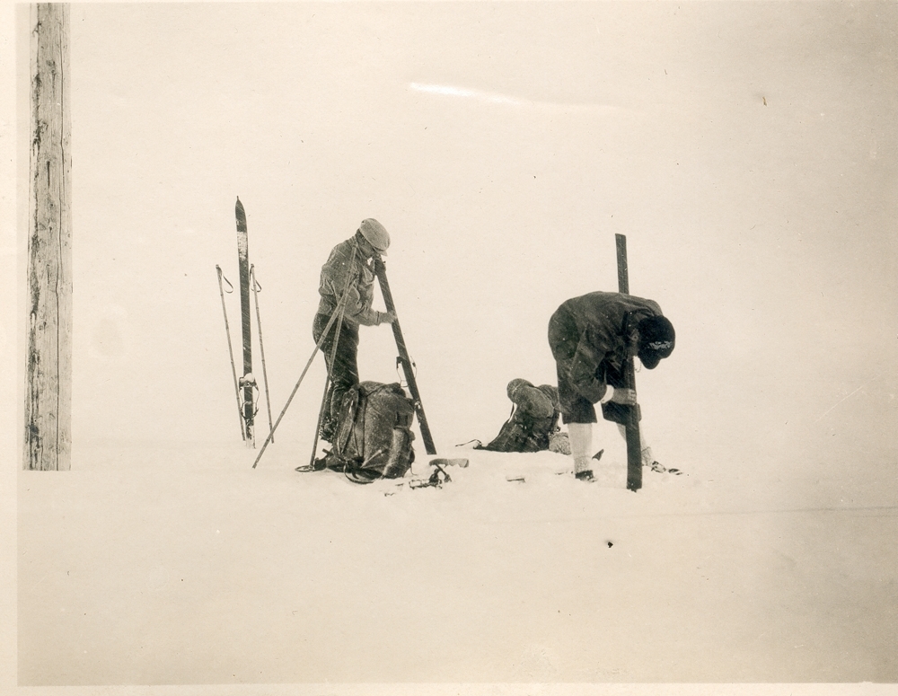To menn smører ski. Telegrafstolpe. Snø.