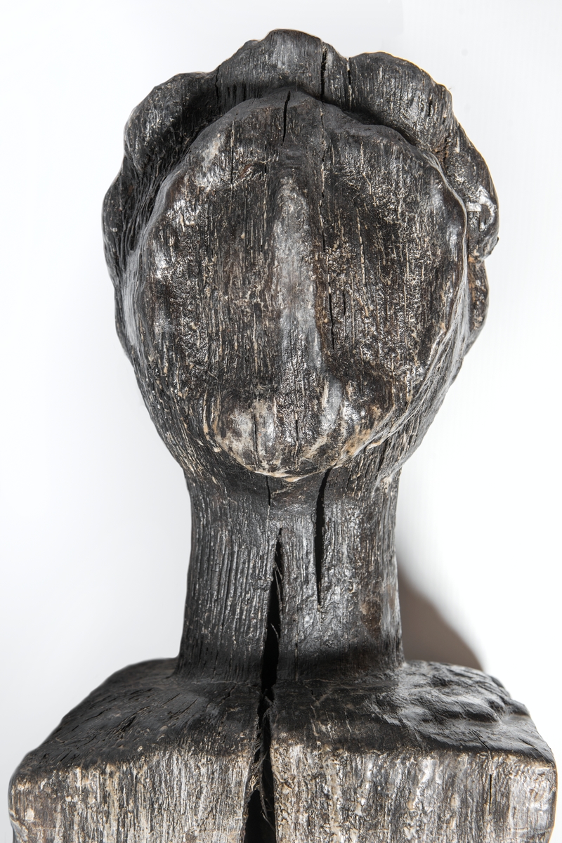 Rektangulär knekt med två skivgatt.
Upptill är knekten krönt med ett tredimensionellt kvinnohuvud med rak, klassisk profil och en konstrik frisyr av romerskt snitt. Huvudet är riktat föröver och snidat i ett med knekten. Runt halsen, på knektens ovansida, är antydan till en bred och platt spetskrage eller liknande. På knektens sidor finns märken efter stora järnbeslag.
Skulpturen är ytsliten men relativt välbevarad.

Text in English: A rectangular knight with two sheave holes.
On top of the knight is a three-dimensional female head with a straight, classical profile and an artistic coiffure of Roman style. The head is carved as part of the knight and faces the bow. Around the neck, on the upper end of the knight, there is a suggestion of a broad flat lace collar or the like. The sides of the knight have marks for large iron fittings.
The sculpture is relatively well preserved despite the worn surface.