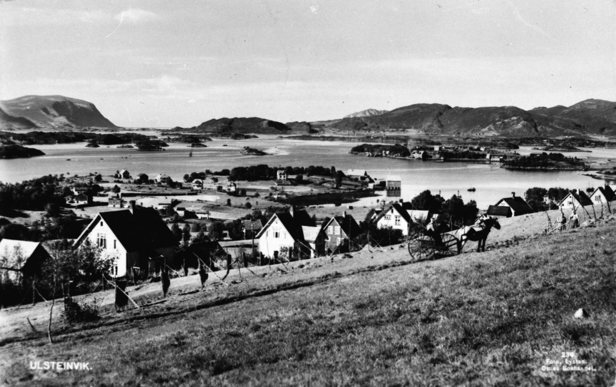 Prospektfotografi av Ulsteinvik med øyene utenfor. I forgrunnen står det noen mennesker og jobber med slåttonn. Hest og kjerre har de med.