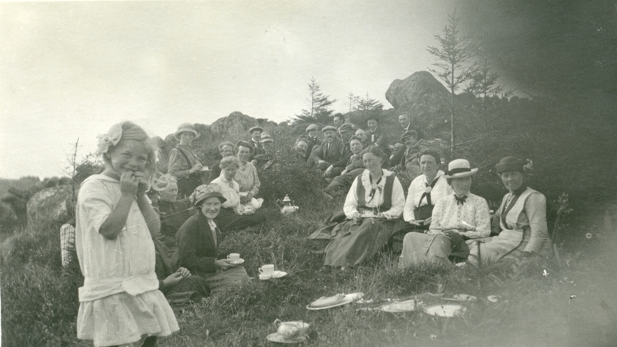 Postkort med en gruppe kvinner, barn og menn har matpause ute i naturen, i forbindelse med besøk hos Arne Garborg, Knudaheio, Time kommune. Dette var i 1916.