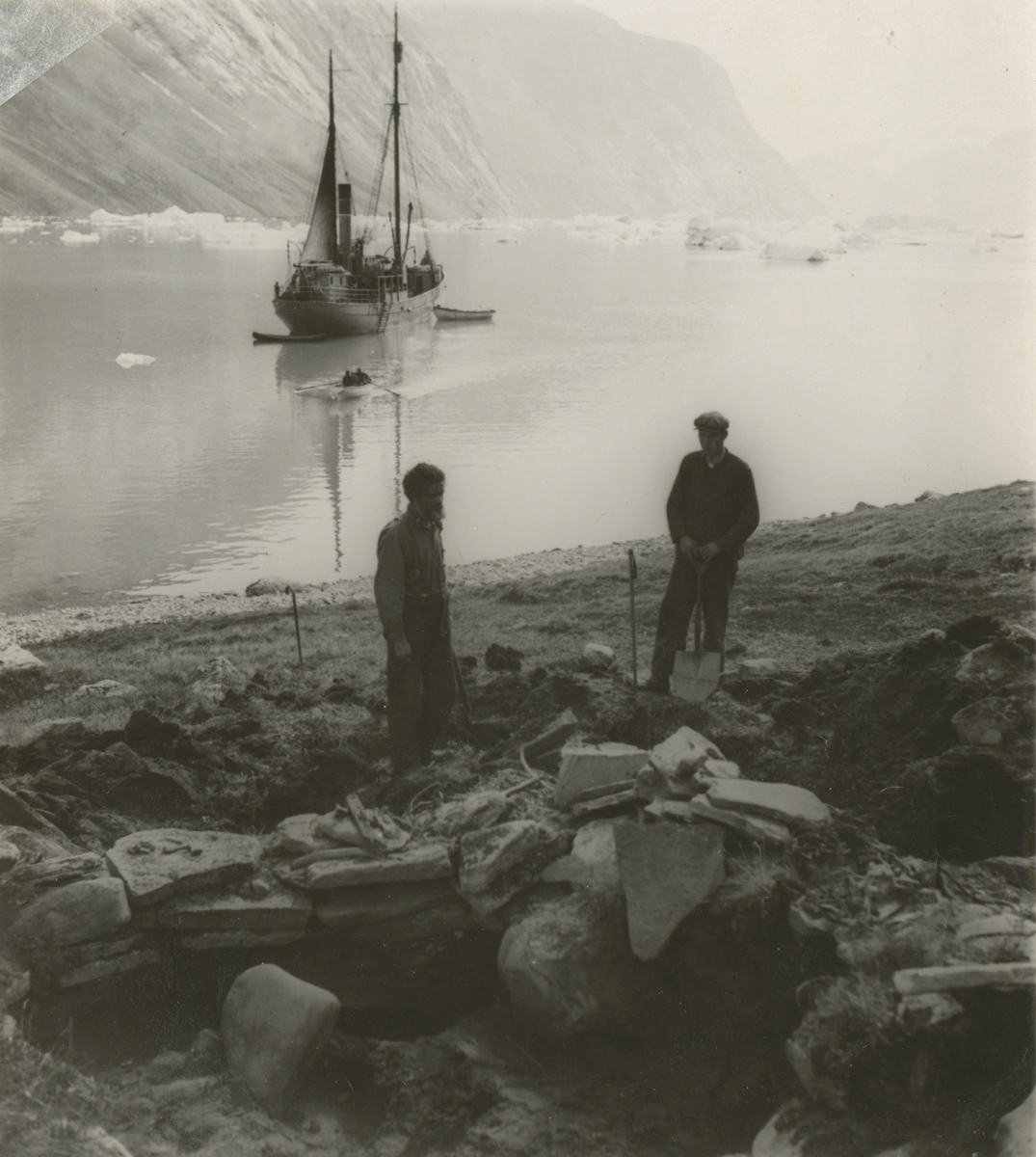Ingvald Skjeldrup gjør utgravinger av et eskimohus sammen med en annen i Reinbukten, Isfjorden på Grønland. Båten Veslekari viser i bakgrunnen.